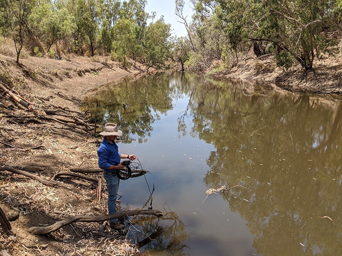 Person standing on bank of Mehi River water monitoring.