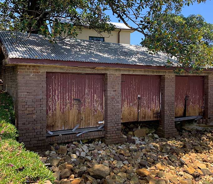 A brick building with three red shed doors, surrounded by rocky terrain and vegetation