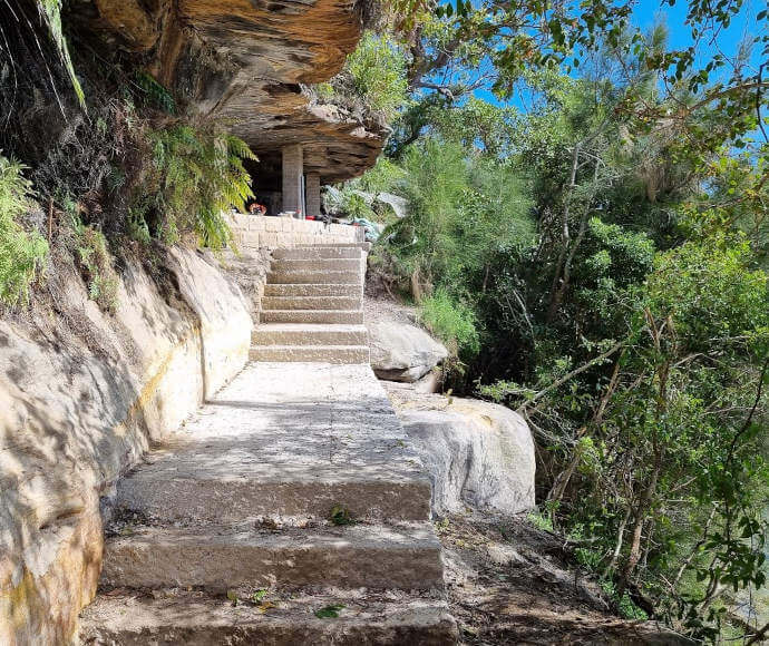Steps cut into stone with small ferns and other foliage beside the path; works underway, Wattamolla Beach Track