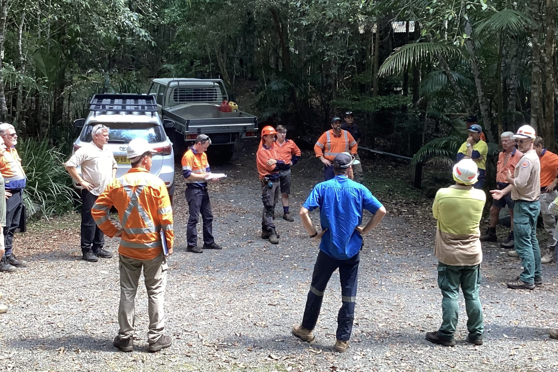 A group of people in high construction appropriate clothing standing in a circle in a car park.