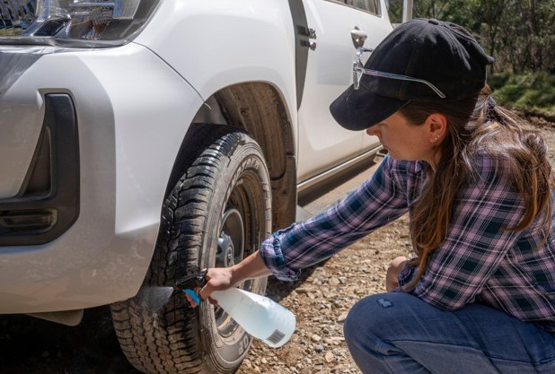 Someone spraying a clear liquid onto the ute wheels. The vehicle wheels are covered in a fine dust from driving on off road conditions. 
