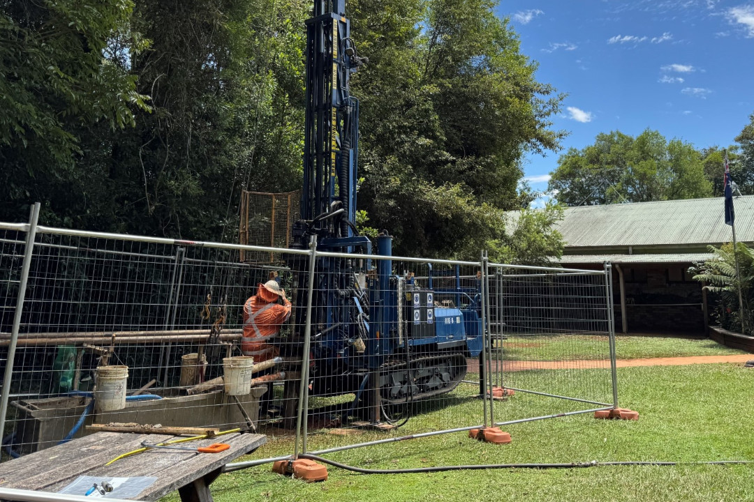 A wire fence on a lawn restricting the access to a large blue drilling machine.